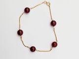 a gold chain bracelet with red glass beads on a white background