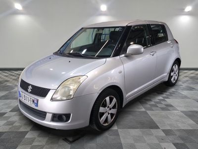 une Suzuki Swift argentée garée sur un sol à damier dans un garage