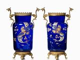 une paire de vases bleus rehaussés de touches dorées, posés sur des socles, sur fond blanc