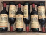 six bottles of red wine in a cardboard box on a table
