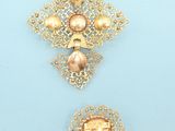 two gold brooches on a blue background, one with pearls and the other with pearls and pearls