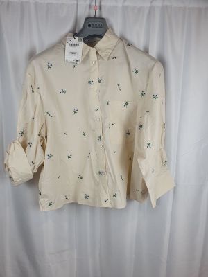 La chemise est suspendue à un cintre devant un rideau blanc.