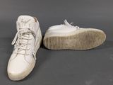 white leather sneakers with laces and rubber soles on a gray surface