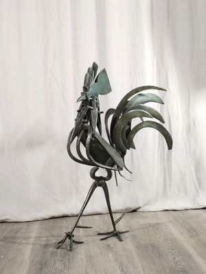une sculpture en métal représentant un coq posée sur un plancher en bois