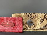 pair of snakeskin purses with metal clasps on a black surface