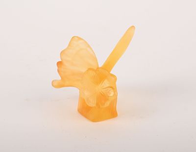 une bougie orange surmontée d'un papillon, posée sur une surface blanche