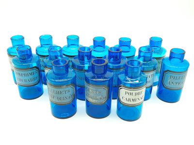 des bouteilles en verre bleues remplies d'un liquide bleu et ornées d'étiquettes argentées sur un fond blanc