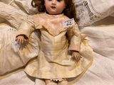 a doll that is sitting on a bed with a lace doily