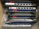 trois trains argentés et bleus se trouvent dans une boîte posée sur une table