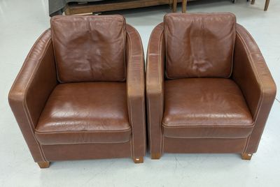 une paire de fauteuils club en cuir marron avec des pieds en bois, dans un magasin