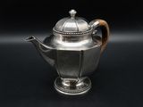 an antique silver teapot with a wooden handle on a black background
