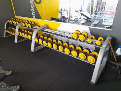 une rangée d'haltères dans une salle de sport, avec une affiche jaune accrochée au mur