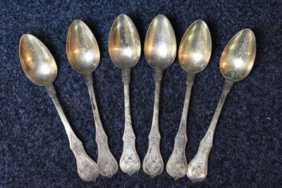 six cuillères en argent sont alignées sur un fond bleu
