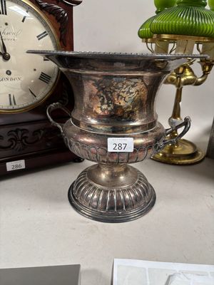 un vase en argent posé sur une table, avec une horloge en arrière-plan