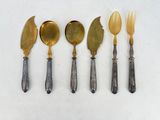 five silver and gold spoons and a knife on a white surface