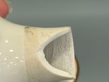 a hand holding a white vase with a hole in it