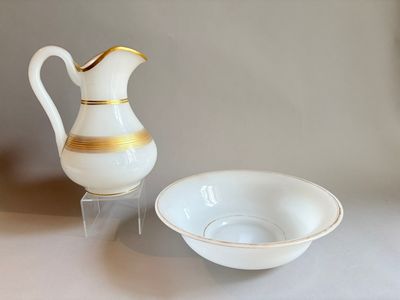 un pichet blanc et doré posé à côté d'un saladier sur une table
