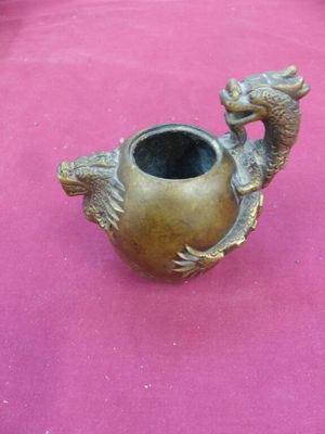 a bronze vase with a dragon on it on a pink surface