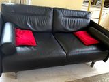 a black leather couch with two red pillows on it