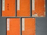 quatre livres orange portant des inscriptions en chinois, posés sur une table