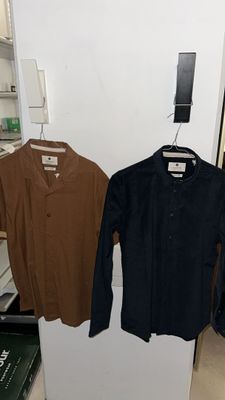 two shirts hanging on a clothes rack in a room