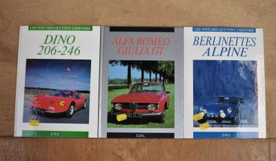 trois livres posés sur une table, avec une voiture rouge et une voiture bleue