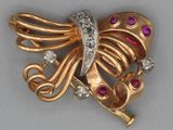 une photo d'une broche en forme de papillon, en or et diamants, posée sur une surface grise