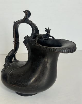 un vase noir muni d'une anse, posé sur une table blanche