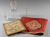a red cloth with a design on it next to a glass