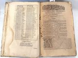 Un vieux livre est ouvert sur une table, sur laquelle se trouvent plusieurs pages.
