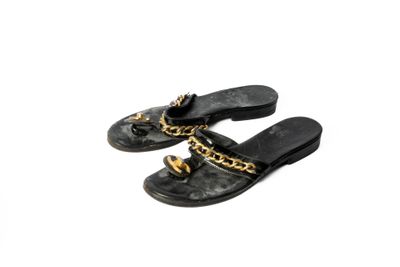une paire de pantoufles noires ornées de chaînes dorées, posées sur un fond blanc