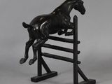 bronze statue of a horse jumping over a wooden fence