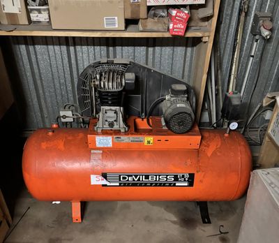 un compresseur d'air orange posé dans un garage à côté d'une pile de cartons