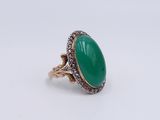 a close up of a ring with a green stone surrounded by diamonds