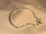 silver chain bracelet on a bed with a white sheet in the background