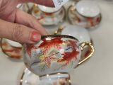 a person that is holding a tea pot in front of a lot of teacups