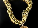 a close up of a gold chain bracelet with a coin on it