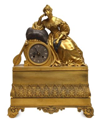 a gold clock with a woman sitting on top of it