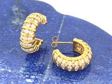 une paire de boucles d'oreilles en forme d'anneaux, de couleur dorée et ornées de cristaux, posée sur une plaque de marbre bleu