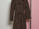 un trench-coat marron suspendu à un cintre devant un mur rose et blanc