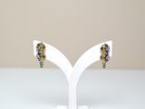 une paire de boucles d'oreilles multicolores posées sur un présentoir blanc, sur une table blanche