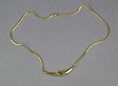 a close up of a gold necklace with a green stone on it