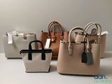 Trois sacs à main sont alignés sur une table, avec des étiquettes accrochées dessus