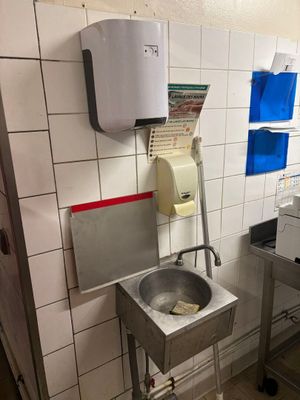 a sink in a public restroom with a paper dispenser on the wall