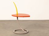 an orange side table with a curved metal base and a yellow flower on top