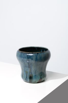 une image représentant un vase bleu posé sur une surface blanche