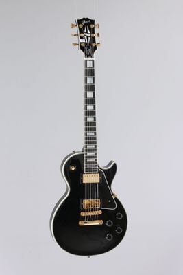 une guitare électrique noire accrochée à un mur blanc