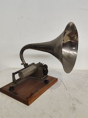 un vieux gramophone argenté posé sur un socle en bois, avec un fond blanc