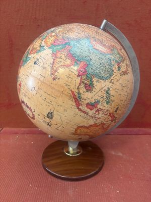 un petit globe sur un support en bois sur une surface rouge