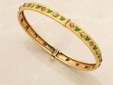 a close up of a gold bracelet with pink and green stones